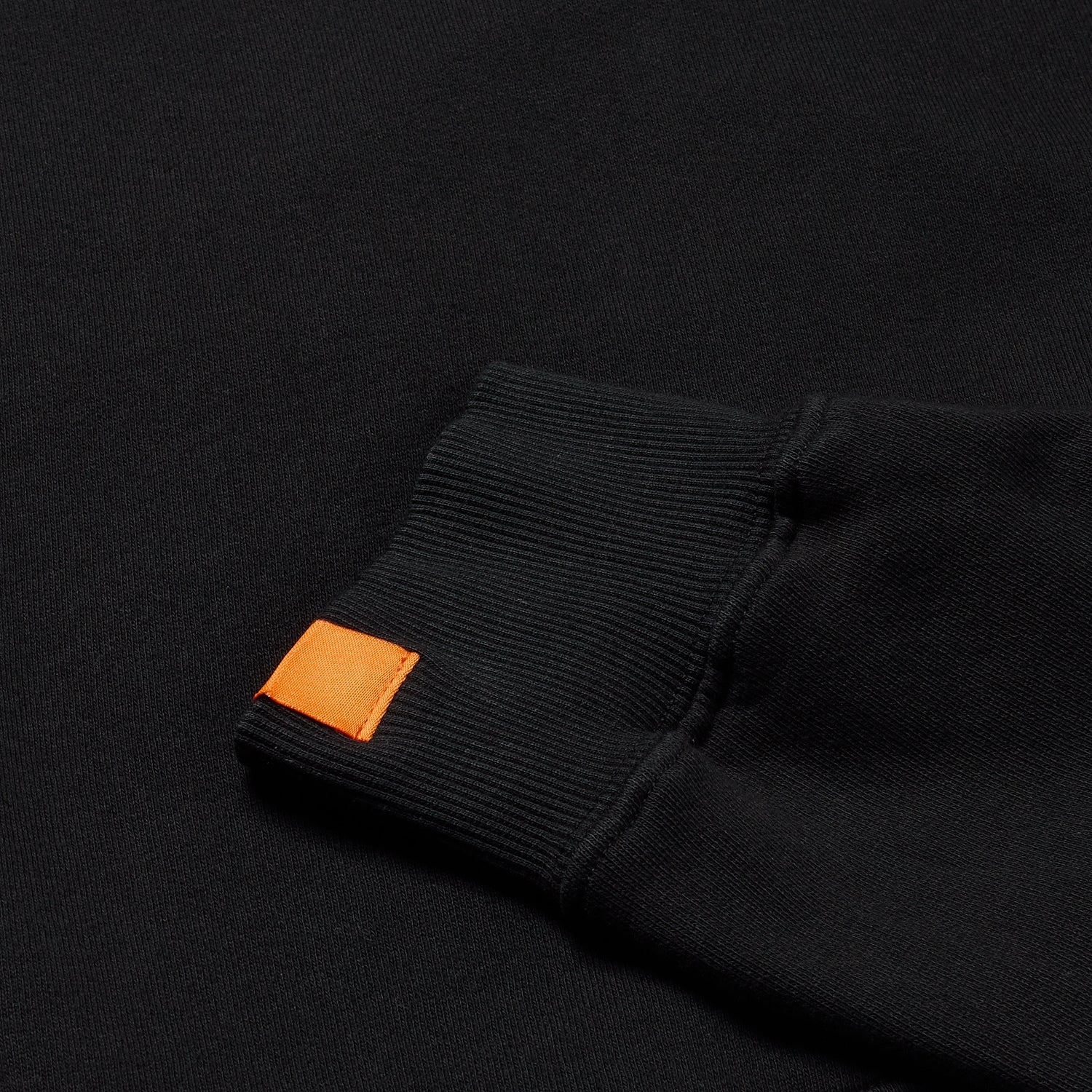 Close-up of black sweatshirt's sleeve showing orange tag detail.