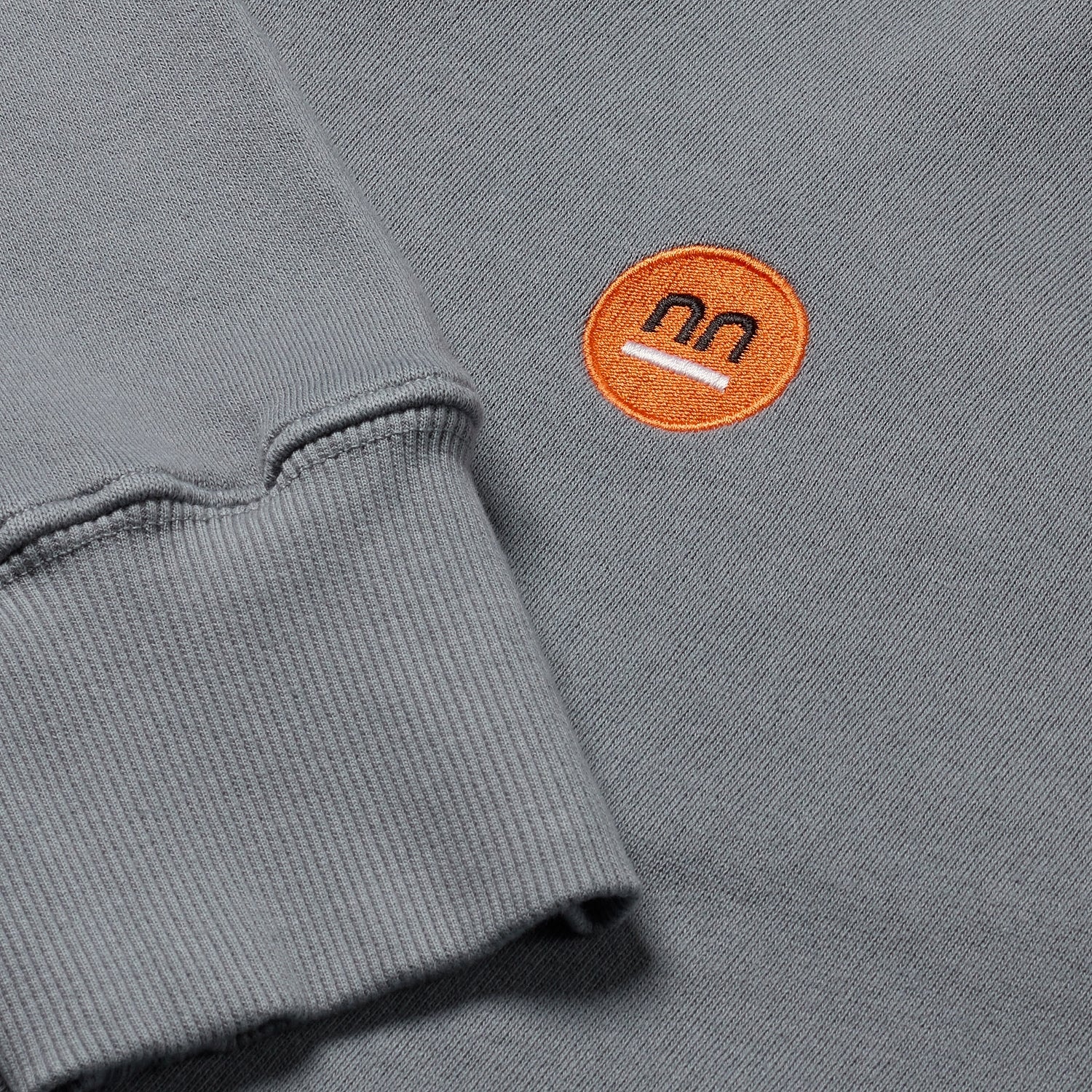 Close-up of grey hoodie's cuff with orange Pamuuc isotope logo.