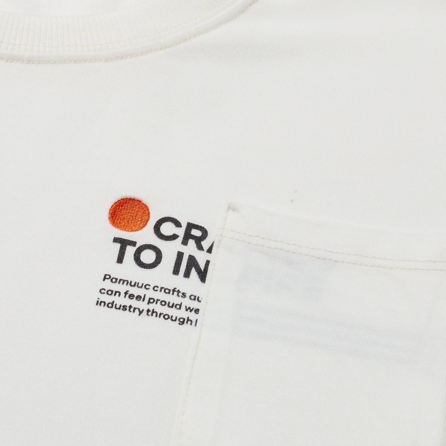 Close-up of white t-shirt's fabric with "Crafted to Inspire" slogan and Pamuuc logo.